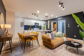 Una sala de estar moderna con un sofá, una mesa de comedor con sillas y una cocina con armarios y electrodomésticos.