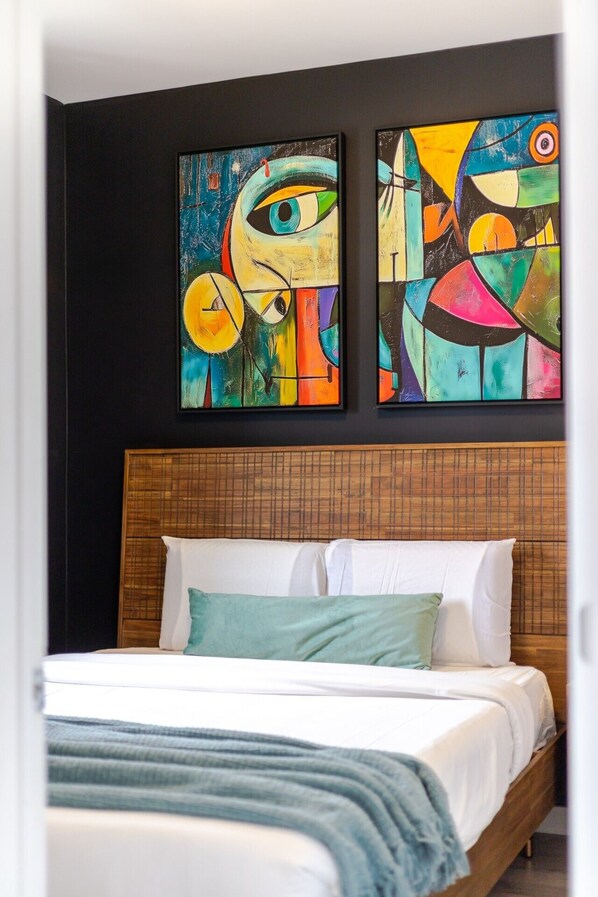 Un dormitorio con una cama, cabecera y dos cuadros abstractos en la pared.