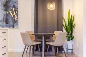 Un comedor con una mesa de vidrio, cuatro sillas, una lámpara colgante y una planta en maceta.
