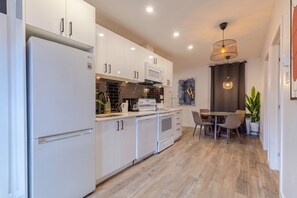 A modern kitchen with white cabinetry, a built-in oven, and a dining area with a table and chairs. - The Perfect Downtown Hideaway (Montréal)
