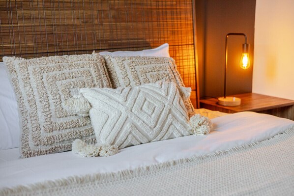 Una cama bien hecha con dos almohadas decorativas, una lámpara de noche y una pared con textura.
