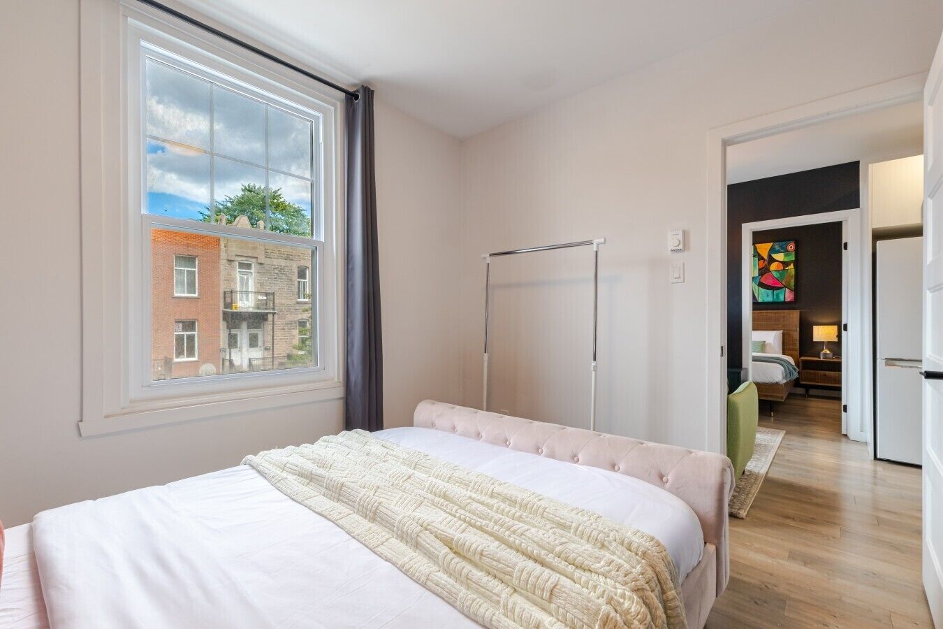 A bedroom with a large window, a bed, a wardrobe, and a view of a building outside.