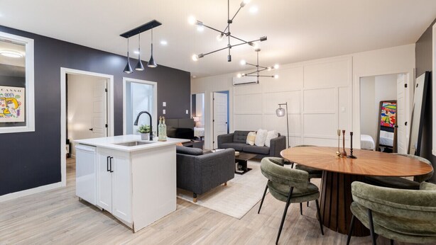 Una cocina moderna con encimera blanca, sofá gris y una mesa de comedor con sillas.