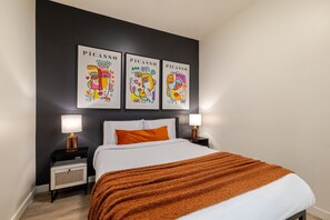 Een slaapkamer met een bed, twee nachtkastjes, en drie kunstwerken van Picasso aan de muur.