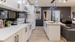 Una cocina moderna con armarios blancos, una estufa y un microondas. Hay una pequeña isla con un fregadero y un televisor.