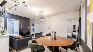 Una sala de estar moderna con una mesa de comedor redonda de madera, sofás grises y un televisor.