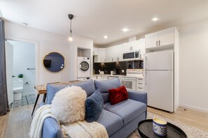A compact living space with a sofa, a coffee table, a kitchen area with appliances, and a laundry room.