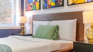Habitación de hotel con una cama, dos lámparas de noche, un almohadón verde y una obra de arte abstracta en la pared.