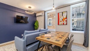 Un salón moderno con un sofá azul, una mesa de centro de madera y un ventanal con vistas a un edificio de ladrillo.