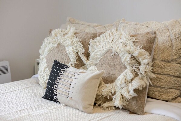 A bed with a textured beige blanket and a white pillow with a black and white pattern.