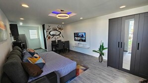 A modern hotel room with a large bed, a dining area, a TV, and a sliding door to the outside.