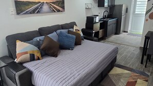 A modern bedroom with a large bed, a desk, and a kitchenette.