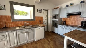 Una cocina moderna con armarios blancos, encimera de madera, horno empotrado y ventana con vistas a la vegetación.