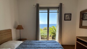 Un dormitorio con cama, lámpara, un cuadro y vista al océano.