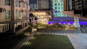 A nighttime view of a modern building complex with multiple high-rise structures, a landscaped courtyard with illuminated pathways, and a pool area with blue lighting. -  A spacious 31sqm studio unit in abreeza place (Davao City)