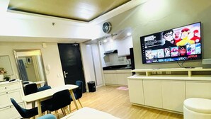 A modern hotel room with a bed, a dining area, a kitchenette, and a TV displaying a movie. -  A spacious 31sqm studio unit in abreeza place (Davao City)