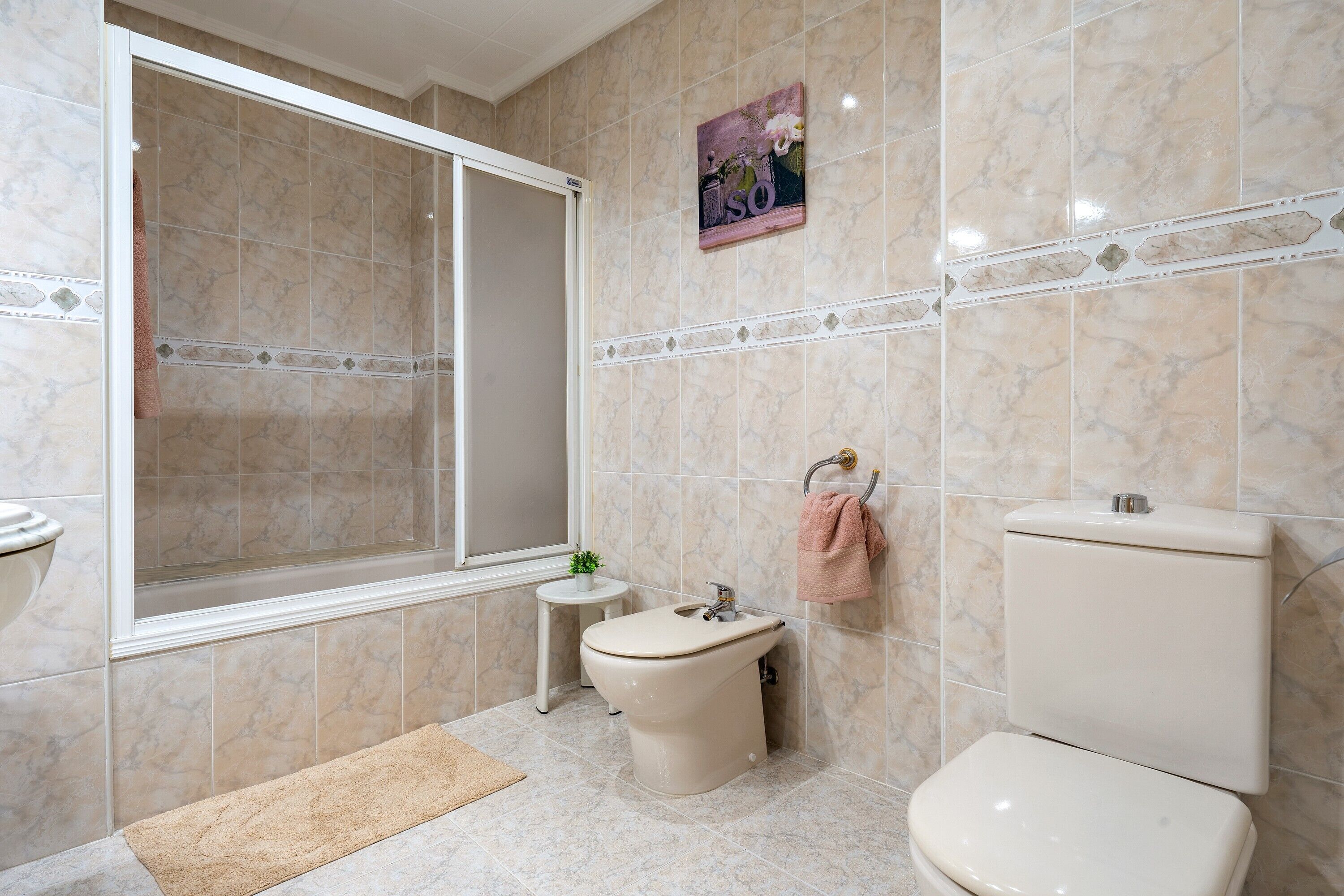 Un baño con ducha, bidé, inodoro y una pequeña mesa con una planta.