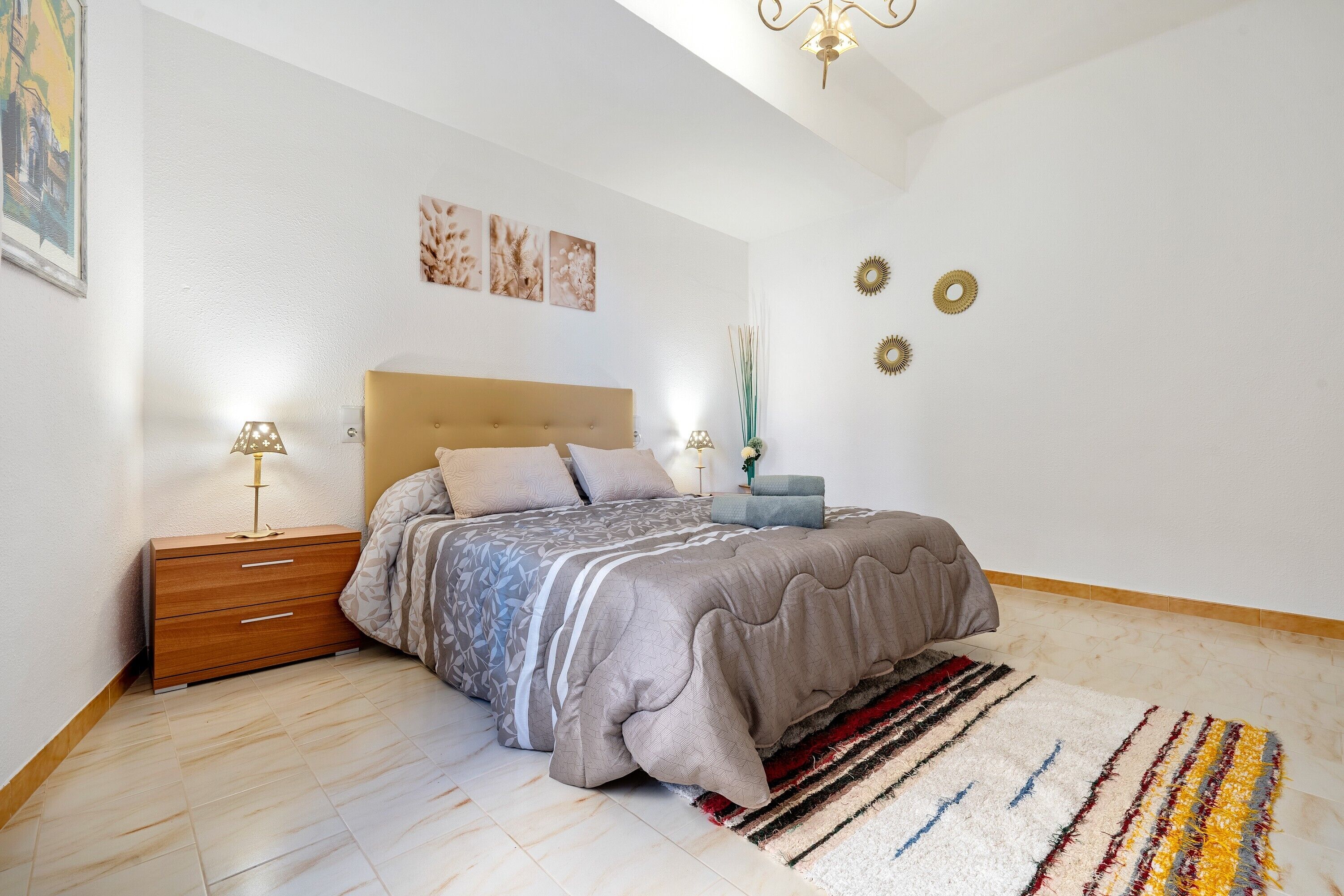 Un dormitorio con cama, mesita de noche, lámpara, decoración en la pared y alfombra.