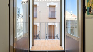 A view through a glass door to a balcony with a tiled floor, metal railings, and a building with multiple windows and balconies in the background. - Apartment 'El Compromiso' with Balcony, Wi-Fi and Air Conditioning (Caspe)