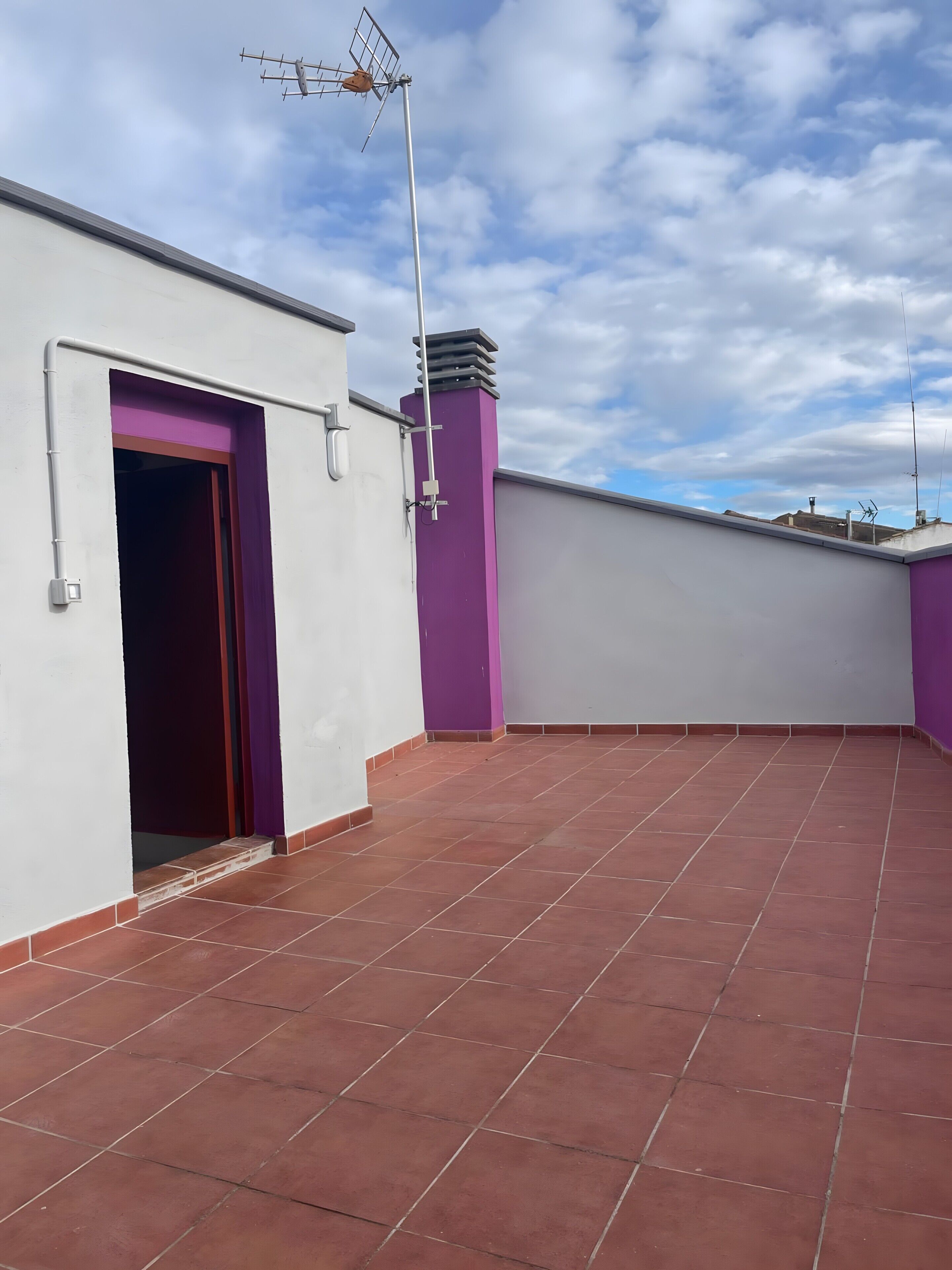 Una terraza en la azotea con techo plano, pared morada y pared blanca con una puerta.