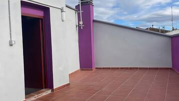 Una terraza en la azotea con techo plano, pared morada y pared blanca con una puerta.