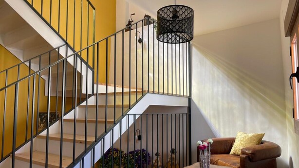 A staircase with metal railings, a brown leather sofa, a small table with vases, and a hanging light fixture. - Country House 'Fe' with Private Terrace, Private Garden and Balcony (Capdesaso)