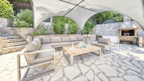 Eine Terrasse im Freien mit Kamin aus Stein, einem Holztisch und einem beigefarbenen Sofa.
