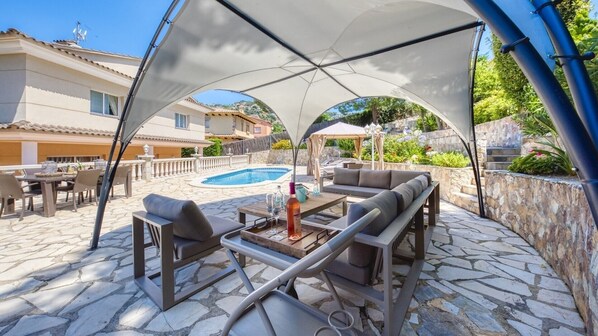 An outdoor patio with a pool, lounge chairs, and a covered seating area.