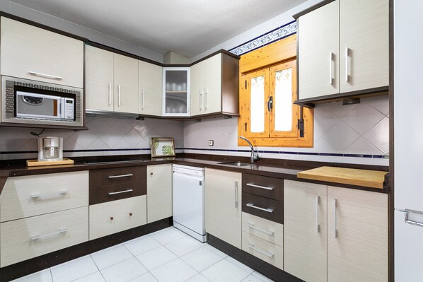 A kitchen with white cabinets, a built-in microwave, a dishwasher, and a wooden window.