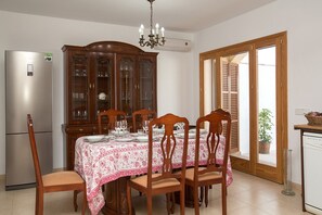 A dining area with a table set for four, a wooden cabinet with glass doors, a refrigerator, and a door leading outside.