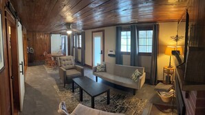 A cozy room with a sofa, armchair, and a small table. There is a window with curtains, a ceiling fan, and a lamp on a side table. - Charming 1-Bedroom, 1-bunk room, fishing in Gate City with Central Air, WiFi (Gate City)
