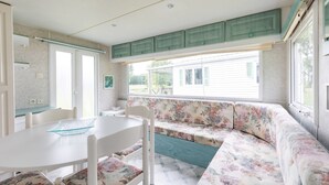 A room with a white table, floral sofa, and green cabinets. - Mobile Home for 3 People at Lake Isachris – Hiking and Relaxation in the Médoc (Queyrac)