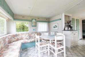 A room with a floral sofa, a round table with chairs, a kitchenette, and a window with a view of greenery.