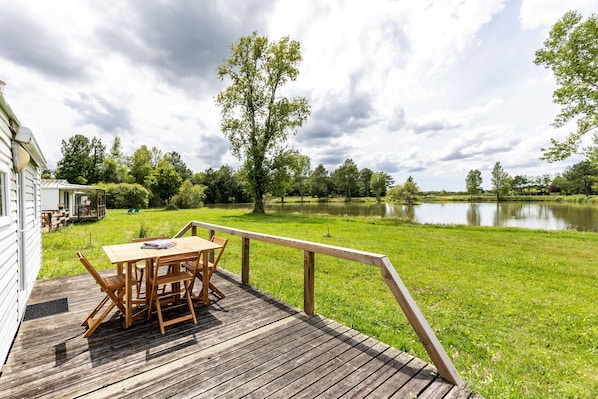 A wooden deck with a table and chairs, overlooking a lake and grassy area.