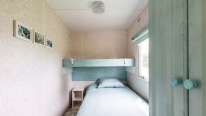 A bedroom with a bunk bed, a small bedside table, and a window. - Mobile Home for 3 People at Lake Isachris – Hiking and Relaxation in the Médoc (Queyrac)