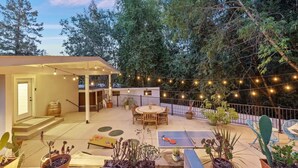 Un patio couvert, agrémenté d’une table et de chaises, entouré de plantes en pot et illuminé de guirlandes lumineuses.