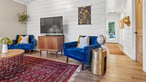 Un salon spacieux avec deux canapés bleus, un meuble en bois, un téléviseur et un tapis rouge à motifs.
