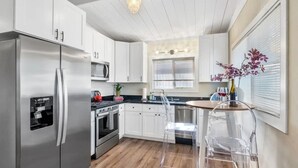Une cuisine moderne avec des meubles blancs, des appareils en acier inoxydable, un plancher en bois et une table en verre transparent.