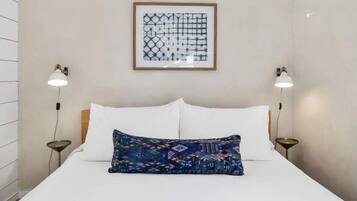 A neatly arranged hotel room with a large bed, two bedside lamps, a framed abstract artwork above the bed, and a patterned throw pillow.