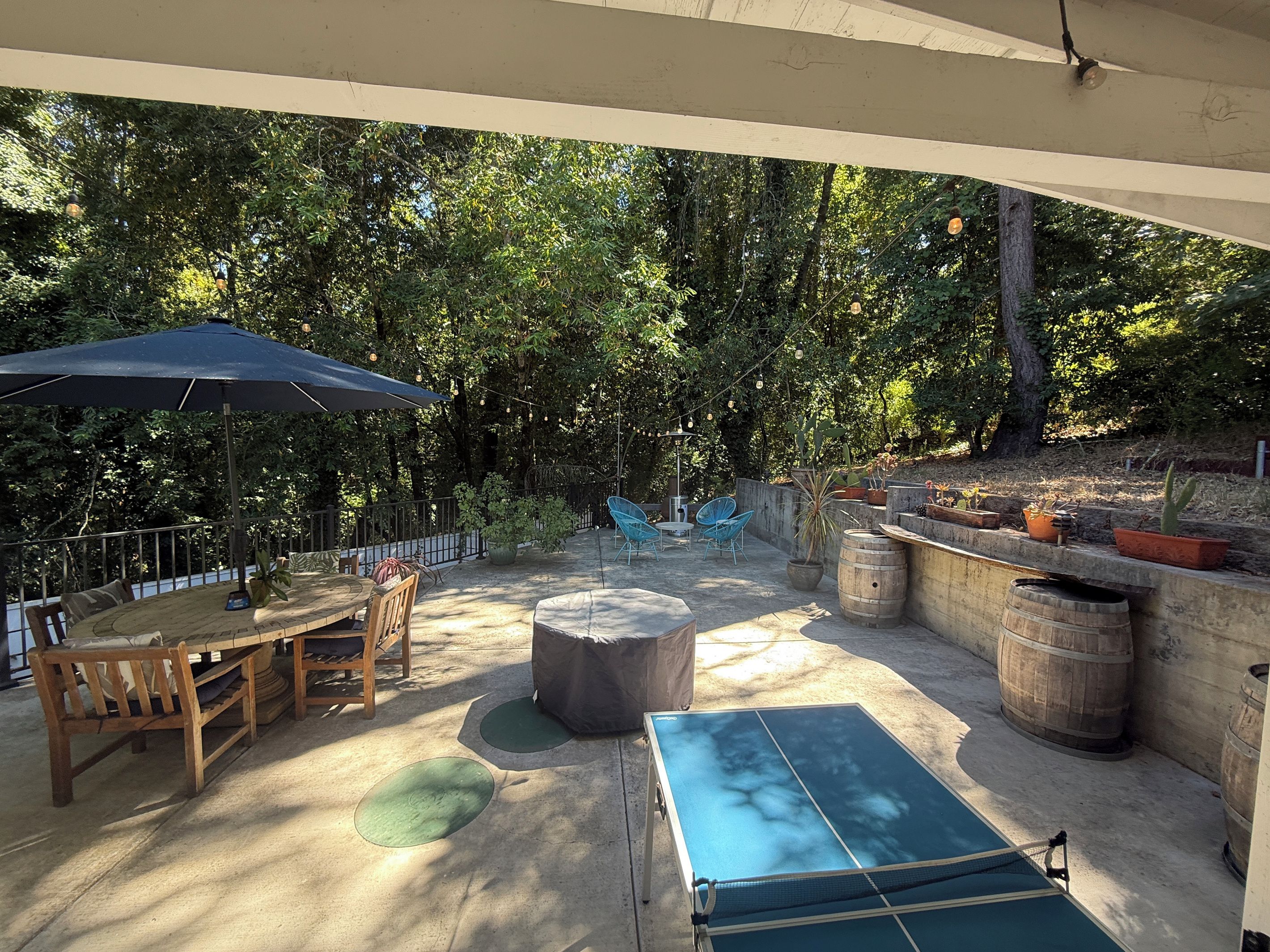 Un patio exterior con mesa de ping pong, asientos y plantas en macetas.