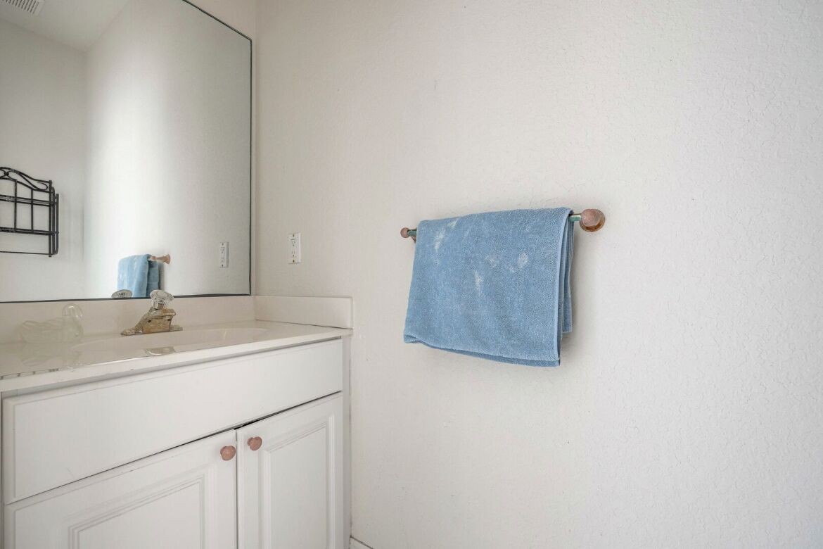 Un baño con un tocador blanco, un espejo y una toalla azul colgada en un perchero de madera.