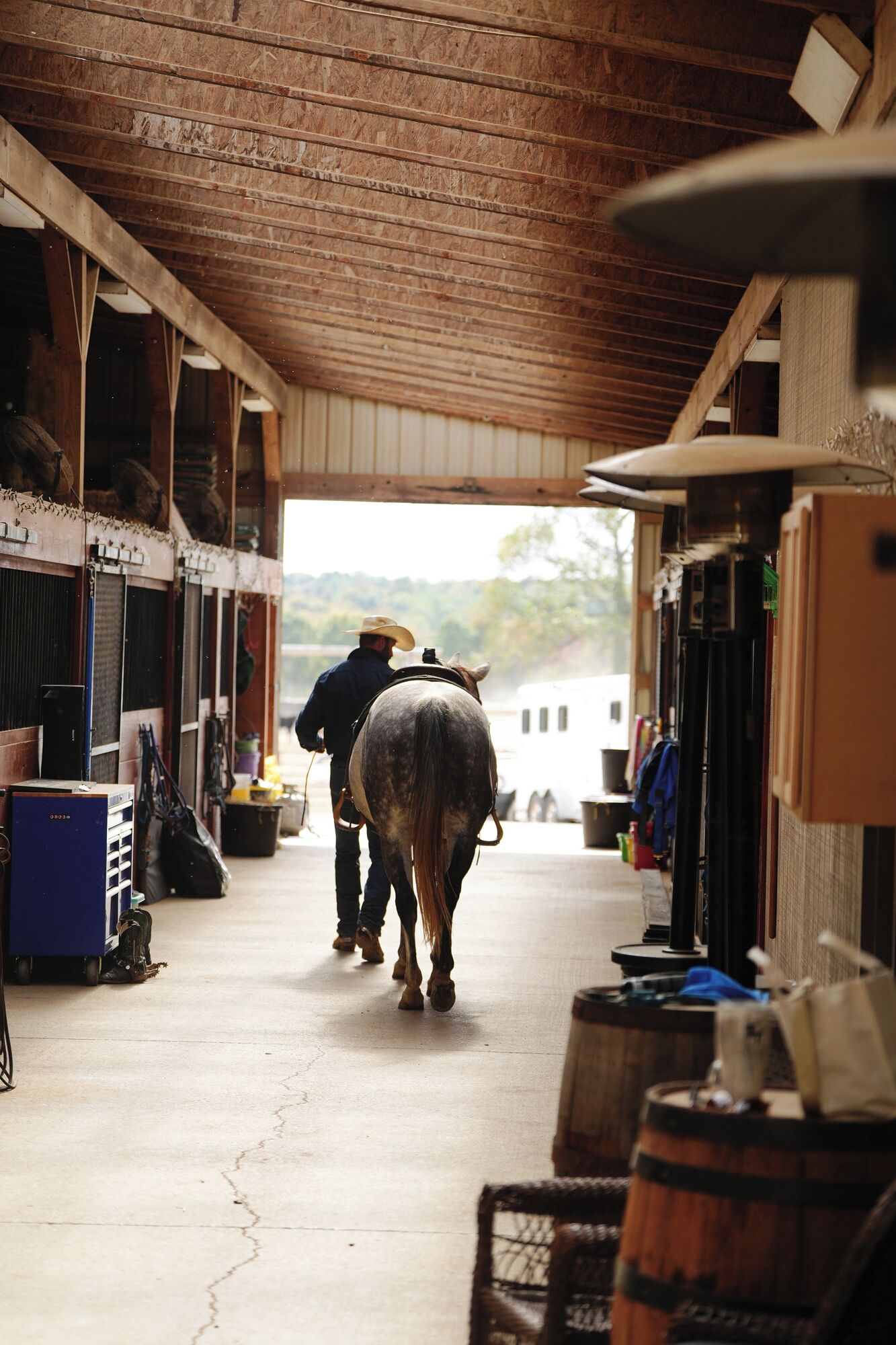 Une écurie abritant un cheval et son cavalier, des boxes en bois et une allée couverte.