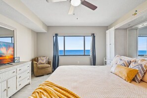 A bedroom with a bed, a ceiling fan, a dresser, a chair, a window with curtains, and a view of the ocean. - Direct Ocean Front Condo Steps to the Beach with Heated pool, Hot tub and Tennis Court! (Cocoa Beach)
