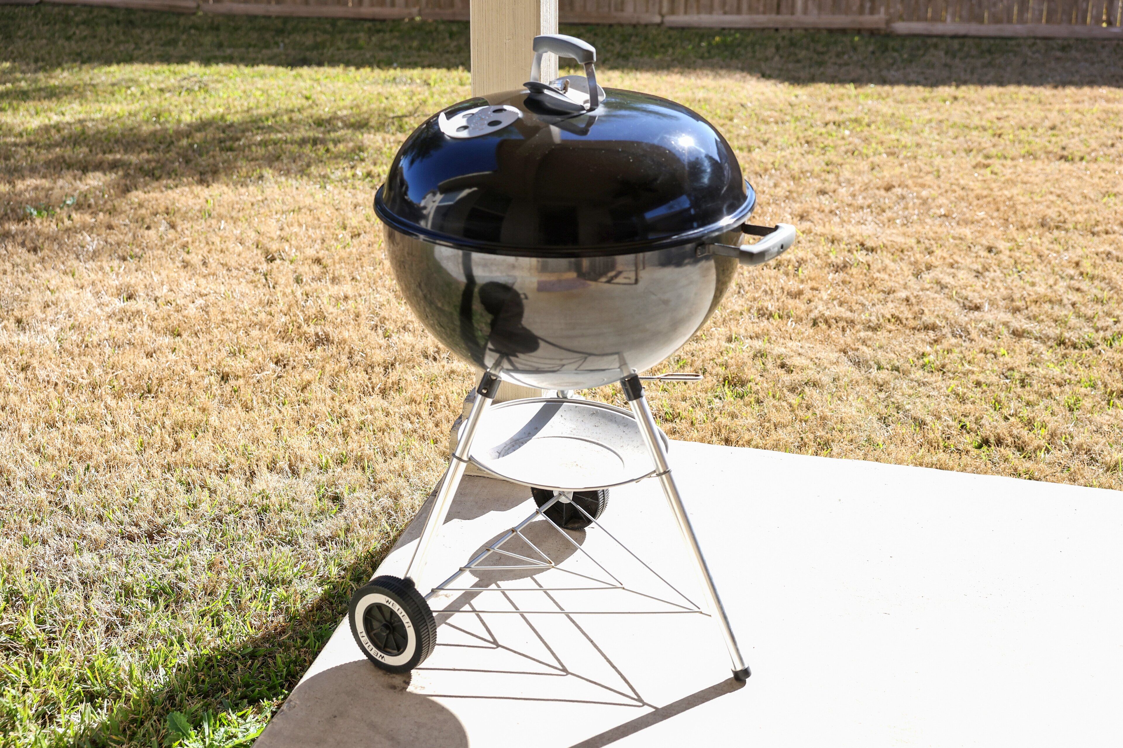 A portable barbecue grill with a lid and wheels, placed on a concrete surface outdoors.