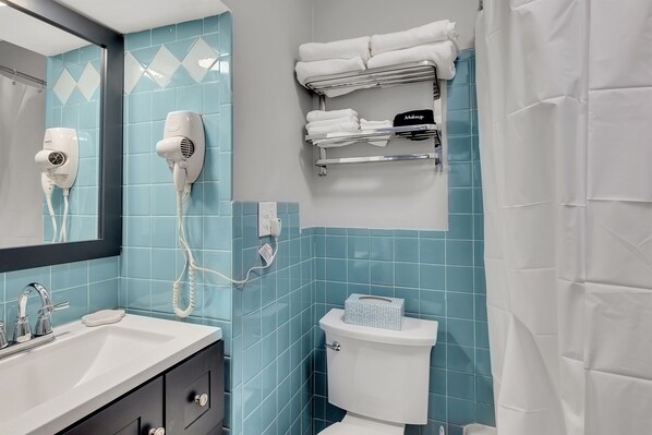 A bathroom with a sink, two hair dryers, a toilet, and a towel rack.