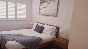 A neatly made bed with a gray throw blanket, white pillows, and a striped pillow. There is a nightstand with a lamp beside the bed. - Beachside Homely Flat in Rockingham (Rockingham)