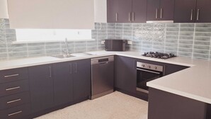 A modern kitchen with dark cabinets, a dishwasher, a stove, and a microwave. - Beachside Homely Flat in Rockingham (Rockingham)