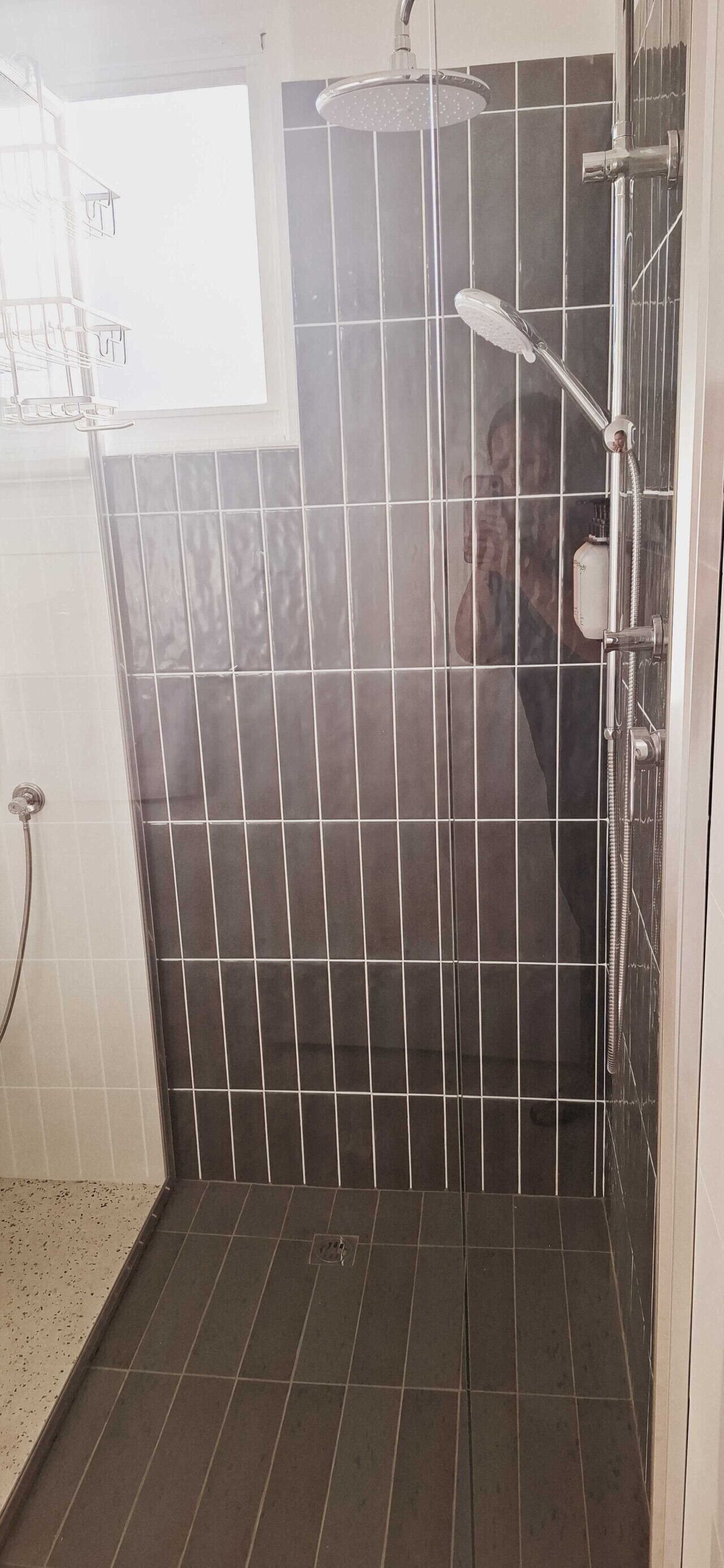 Suihkutila, jossa on tummat laattaseinät ja näkyvissä oleva suihkupää.
