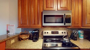 A kitchen with wooden cabinets, a stainless steel microwave, a stove, and a coffee maker. - Luxury Studio | In Town | Wi-Fi | The Grande 312 (Angel Fire)