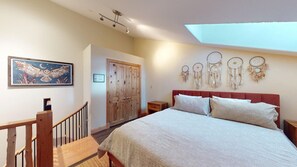 A bedroom with a bed, a wooden wardrobe, a nightstand, a framed picture, and dreamcatchers on the wall.